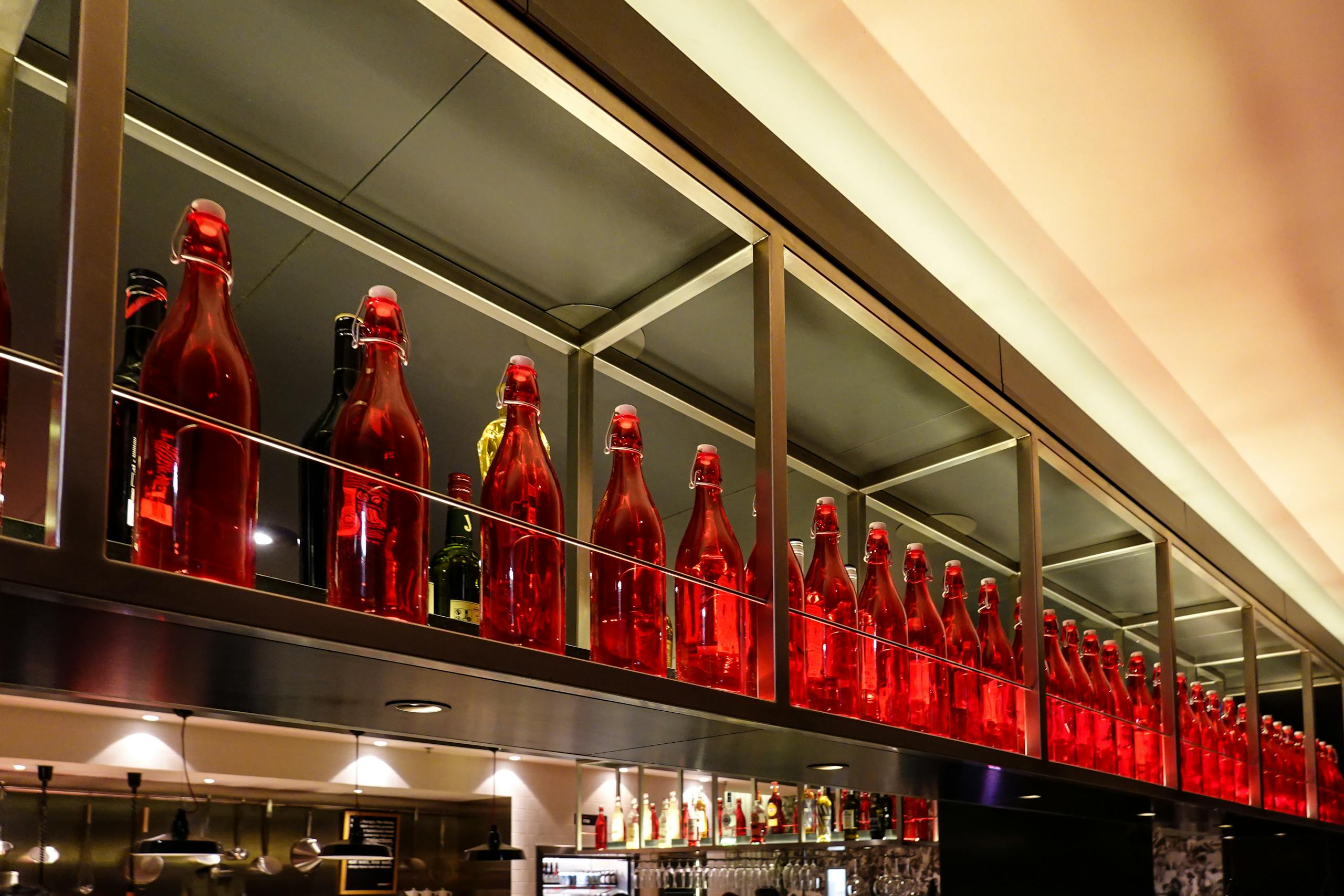 Elegant display of red glass bottles on a bar shelf in a modern restaurant setting.