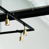 Stylish gold pendant lamps hang from a black metal frame in a modern, minimalist interior.